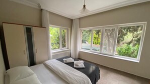 A bedroom with a bed, a wardrobe, and large windows with a view of greenery. - Büyükada Apart Hotel - Karadağ Apart (Adalar)