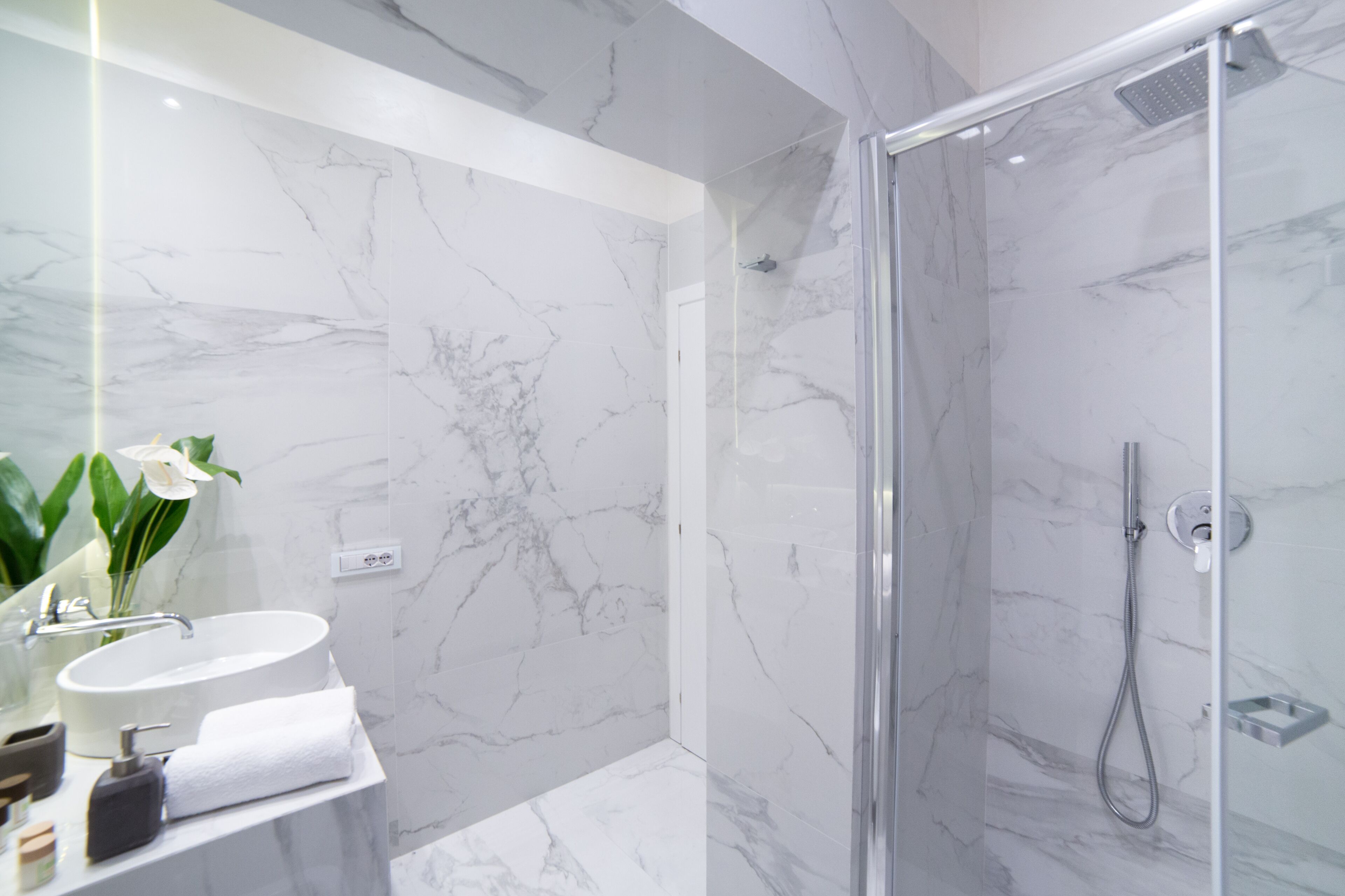 A modern bathroom with a marble sink, a glass shower enclosure, and a large mirror.