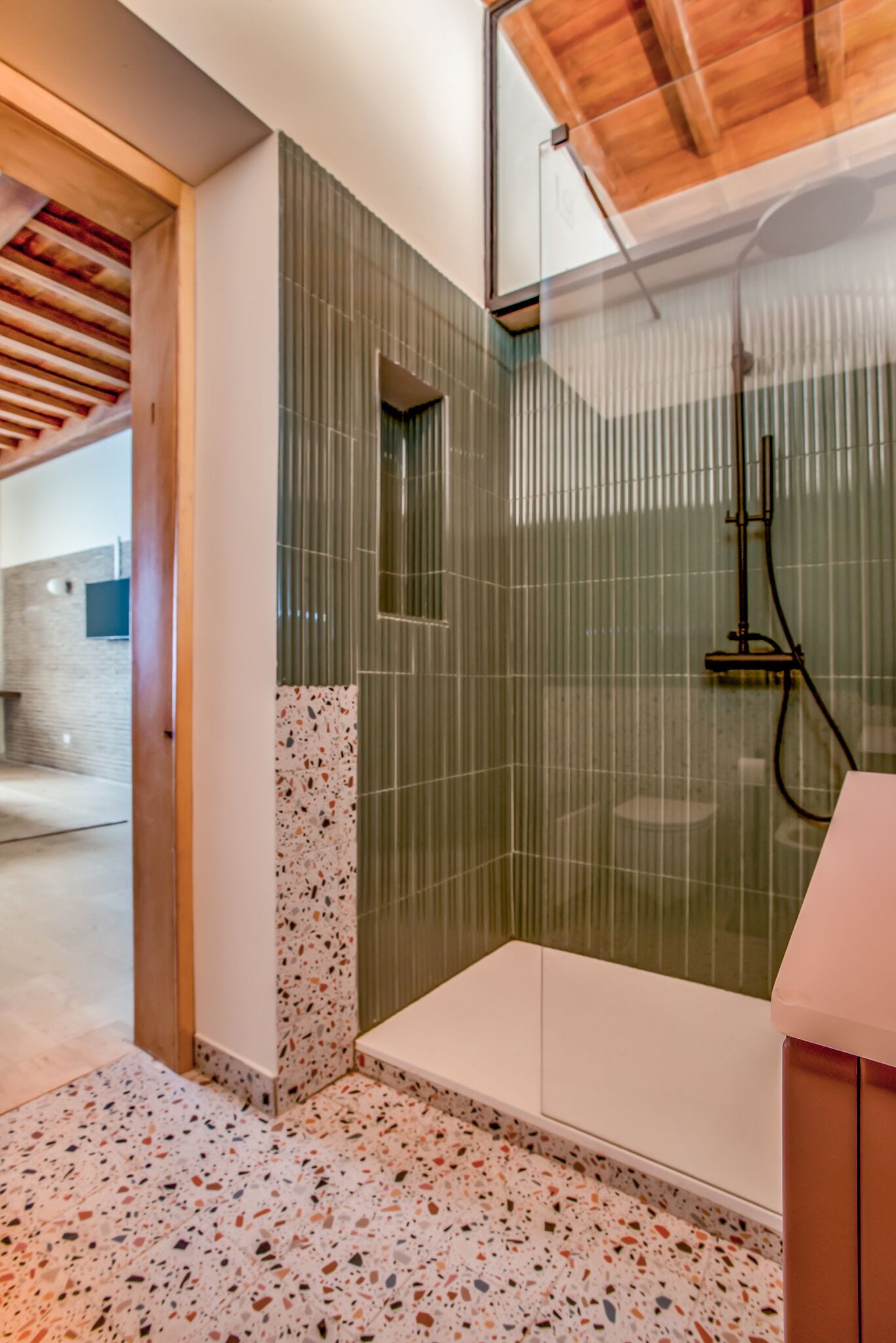 Une salle de bain moderne avec une douche, une petite fenêtre et un sol en terrazzo.