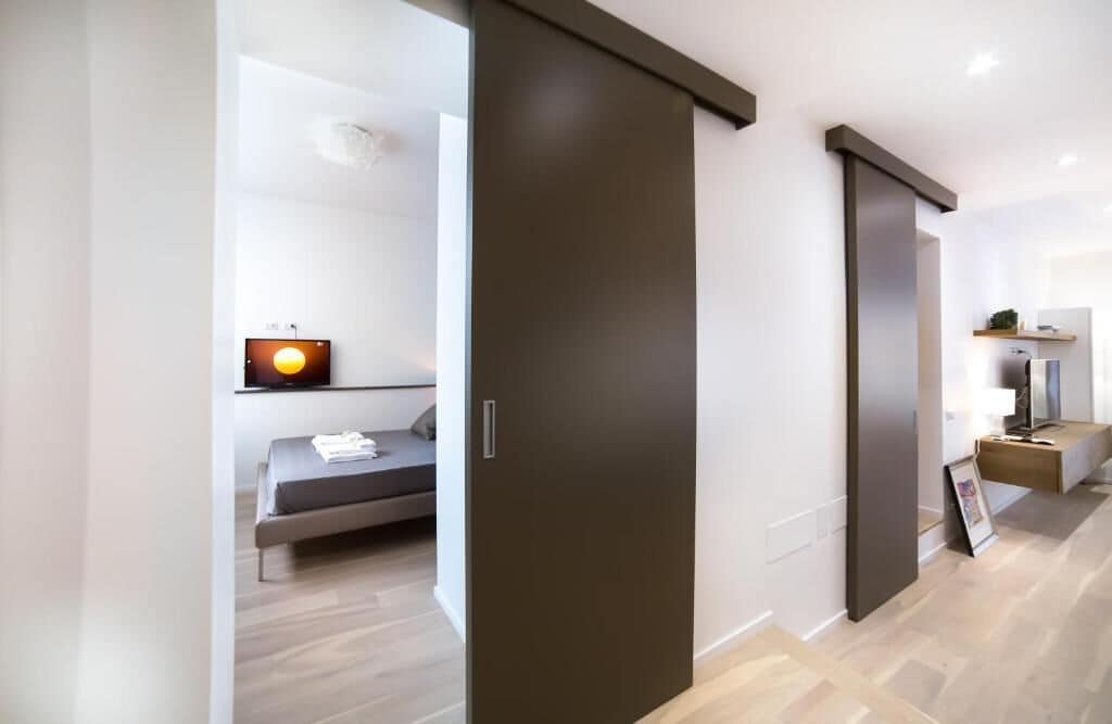 A modern interior with a sliding door leading to a bedroom with a bed, a bedside table, and a wall-mounted TV.