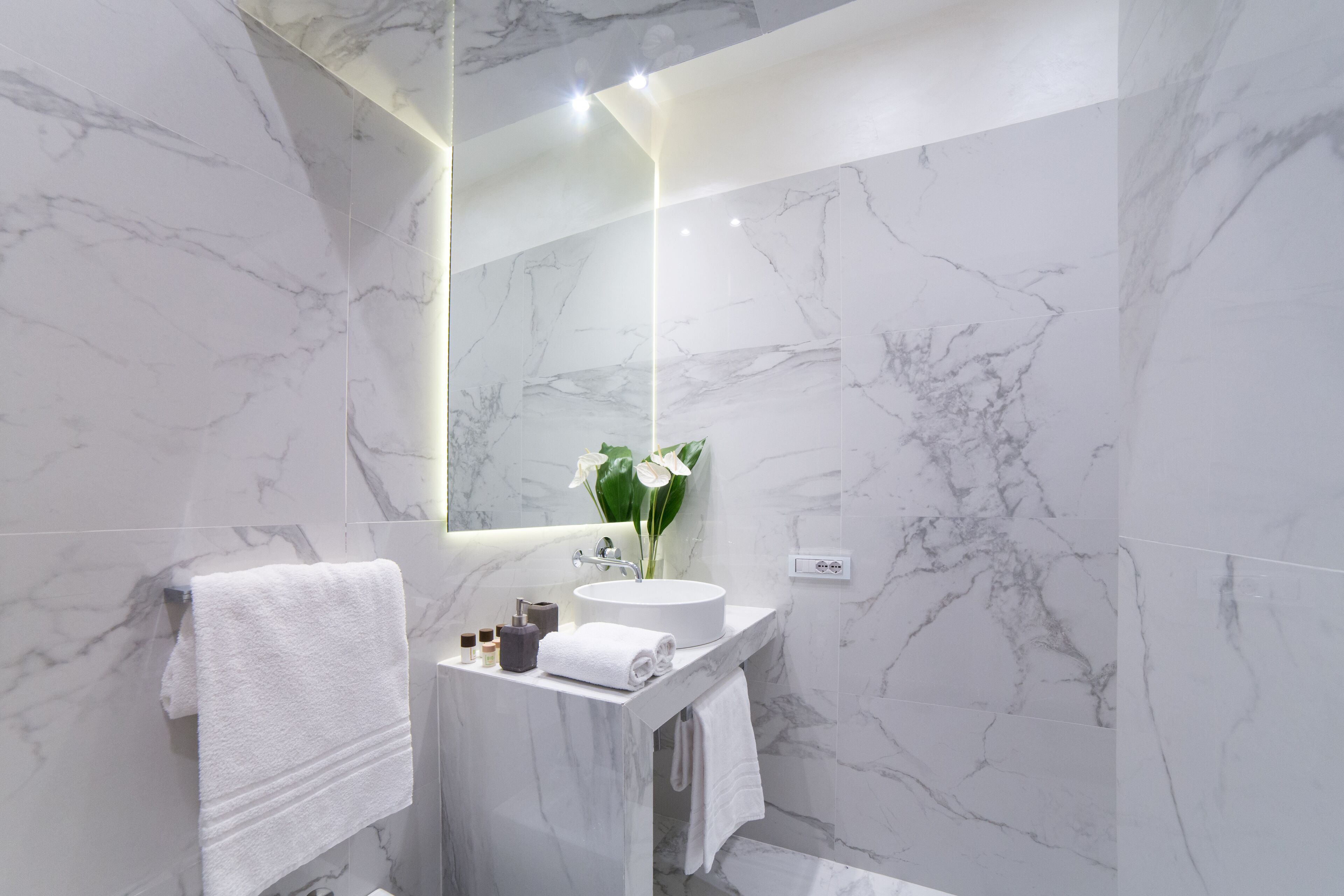 A modern bathroom with marble walls, a round sink, and a large mirror.