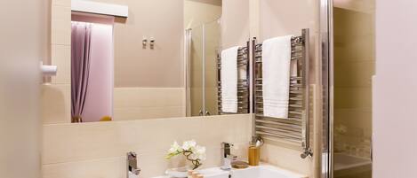 A modern bathroom with a large mirror, two sinks, a glass shower enclosure, and a towel rack with multiple towels.