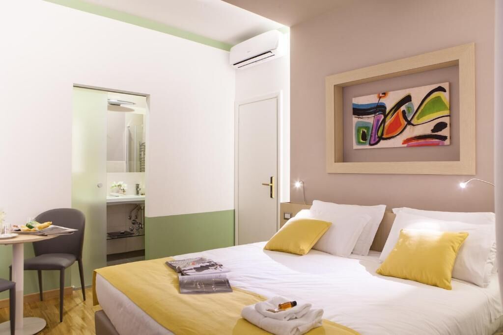 Quarto de hotel com cama, escrivaninha, cadeira e banheiro visível por uma porta aberta.