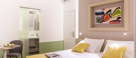 Quarto de hotel com cama, escrivaninha, cadeira e banheiro visível por uma porta aberta.