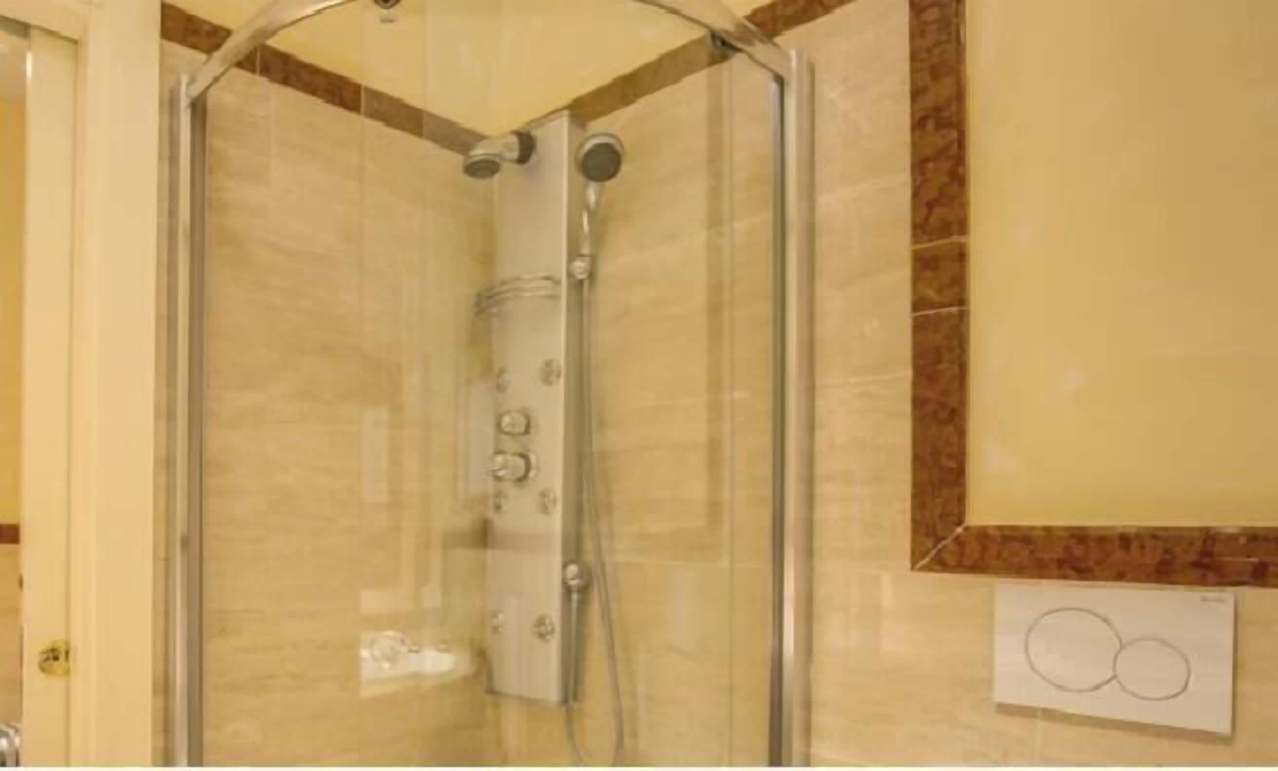 A glass-enclosed shower with a control panel, beige tiles, and a marble accent wall.