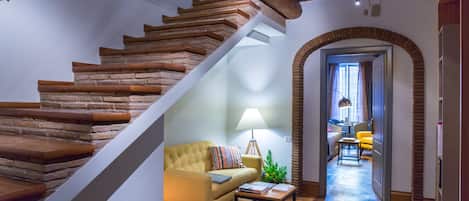 Una escalera con escalones de madera y diseño moderno que conduce a una sala de estar con un sofá, una lámpara y una mesita.