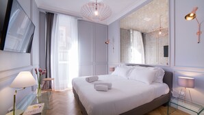 Een moderne slaapkamer met een groot bed, een flatscreen televisie, een glazen bijzettafeltje en een spiegel.