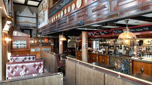 A bar area with wooden paneling, a bar counter, and seating with cushioned booths.