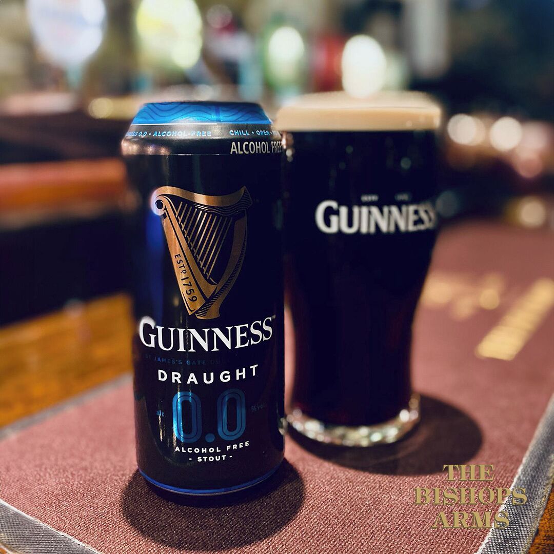 A Guinness Draught can and a glass of beer on a bar counter.