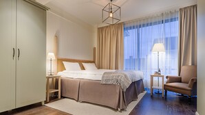 A hotel room with a bed, a chair, a nightstand, a lamp, and a window with curtains.