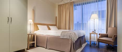 A hotel room with a bed, a chair, a nightstand, a lamp, and a window with curtains.