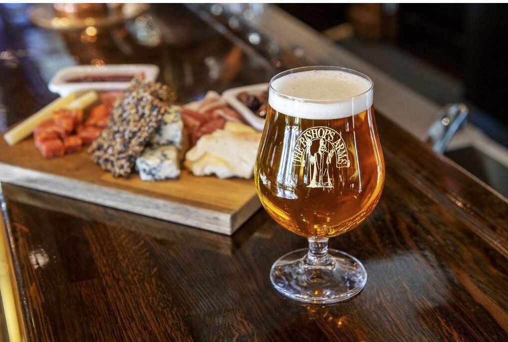 Un verre de bière posé sur le comptoir en bois d’un bar, avec une planche de charcuterie en arrière-plan.