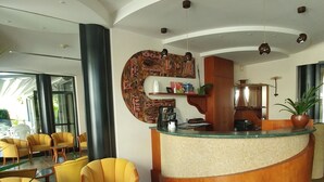 Un hall con mostrador de recepción, sillas amarillas, una mesita y una planta en maceta.
