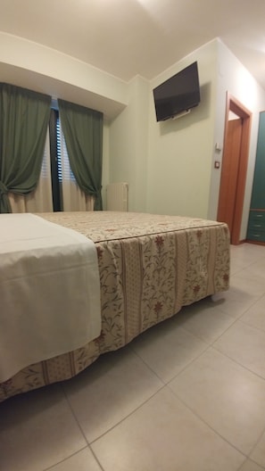 A bedroom with a bed, a TV mounted on the wall, and a door leading to another room. - Hotel La Perla (Roseto degli Abruzzi)