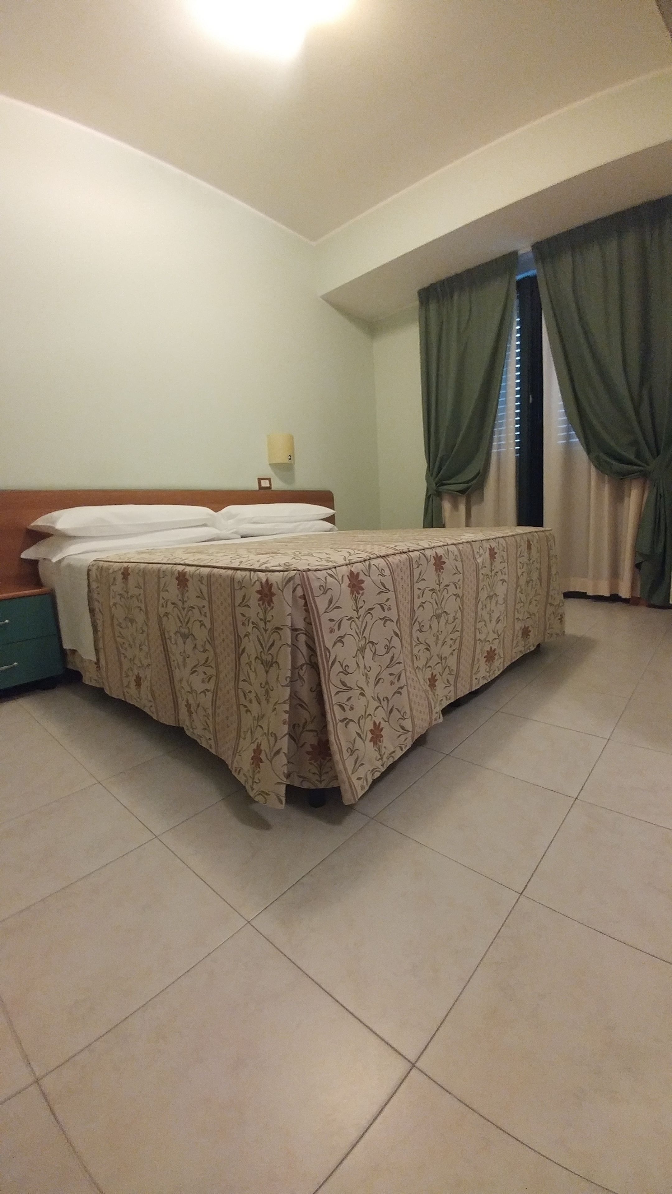 A bedroom with a bed, a nightstand, a lamp, and a window with curtains.