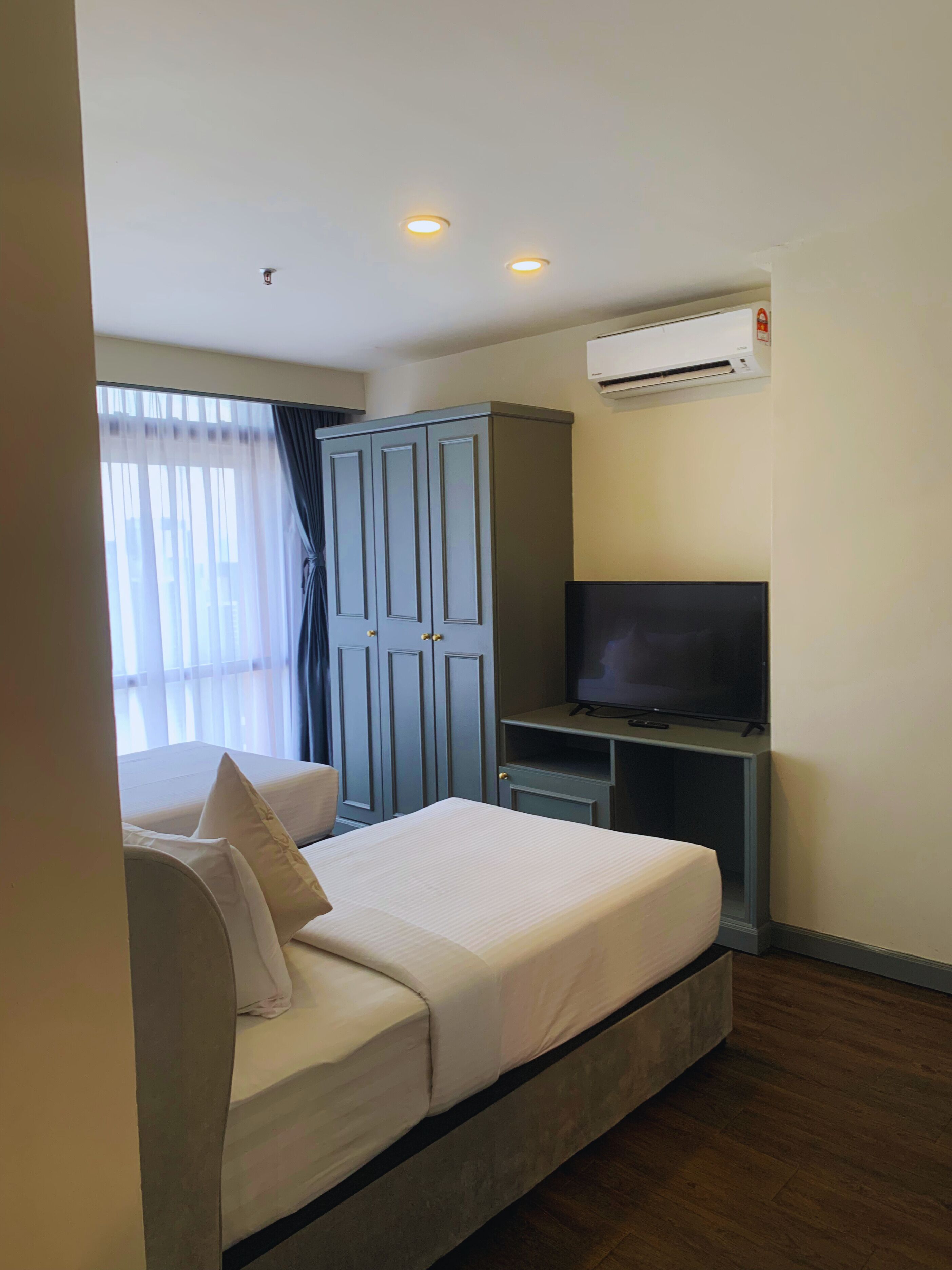 Habitación de hotel con cama, televisor, armario y aire acondicionado.