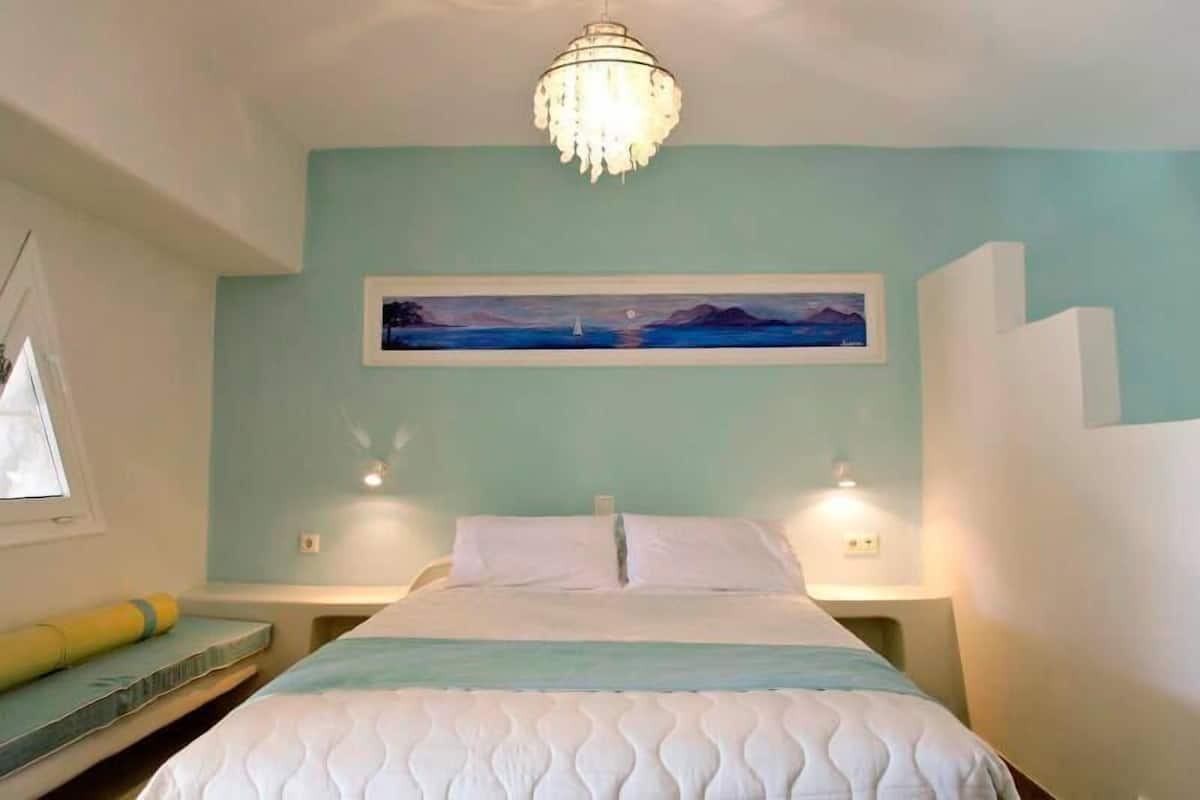 A bedroom with a bed, a painting, a chandelier, and bedside lamps.