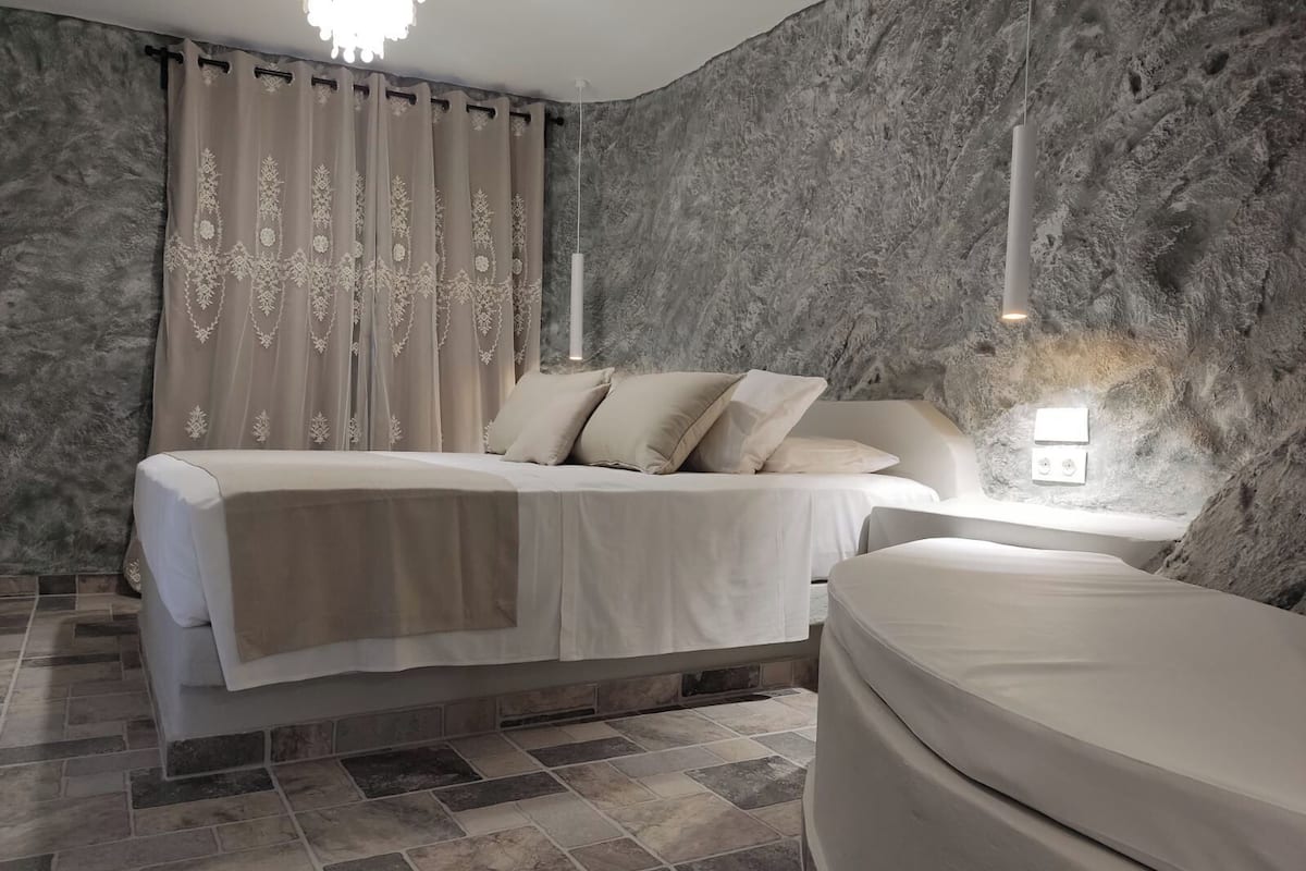A modern bedroom with a large bed, a bedside table, and a wall-mounted light.