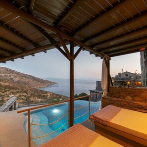 A pool area with a view of the sea and mountains, wooden deck, and a stone wall. - Aegean Castle  Andros - Adults Only (Andros)