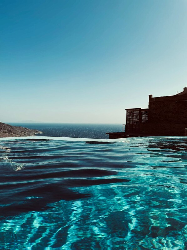 Una piscina azul cristalina con vista al océano y un edificio de piedra.