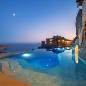 Una piscina infinita con vistas al mar y un edificio de arquitectura de piedra.