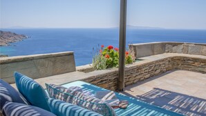A sunlit outdoor seating area with a view of the sea, stone walls, and a stone bench. - Aegean Castle  Andros - Adults Only (Andros)