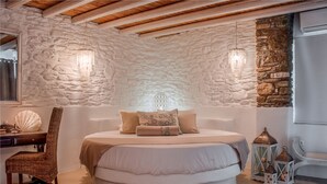A bedroom with a stone wall, a round bed, a wooden chair, and two hanging lights. - Aegean Castle  Andros - Adults Only (Andros)