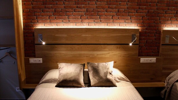 A bed with a wooden headboard against a brick wall, two bedside tables, and a light fixture above the headboard. - Hôtel des Pyrénées (Paris)