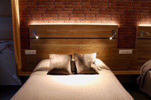 A bed with a wooden headboard against a brick wall, two bedside tables, and a light fixture above the headboard. - Hôtel des Pyrénées (Paris)