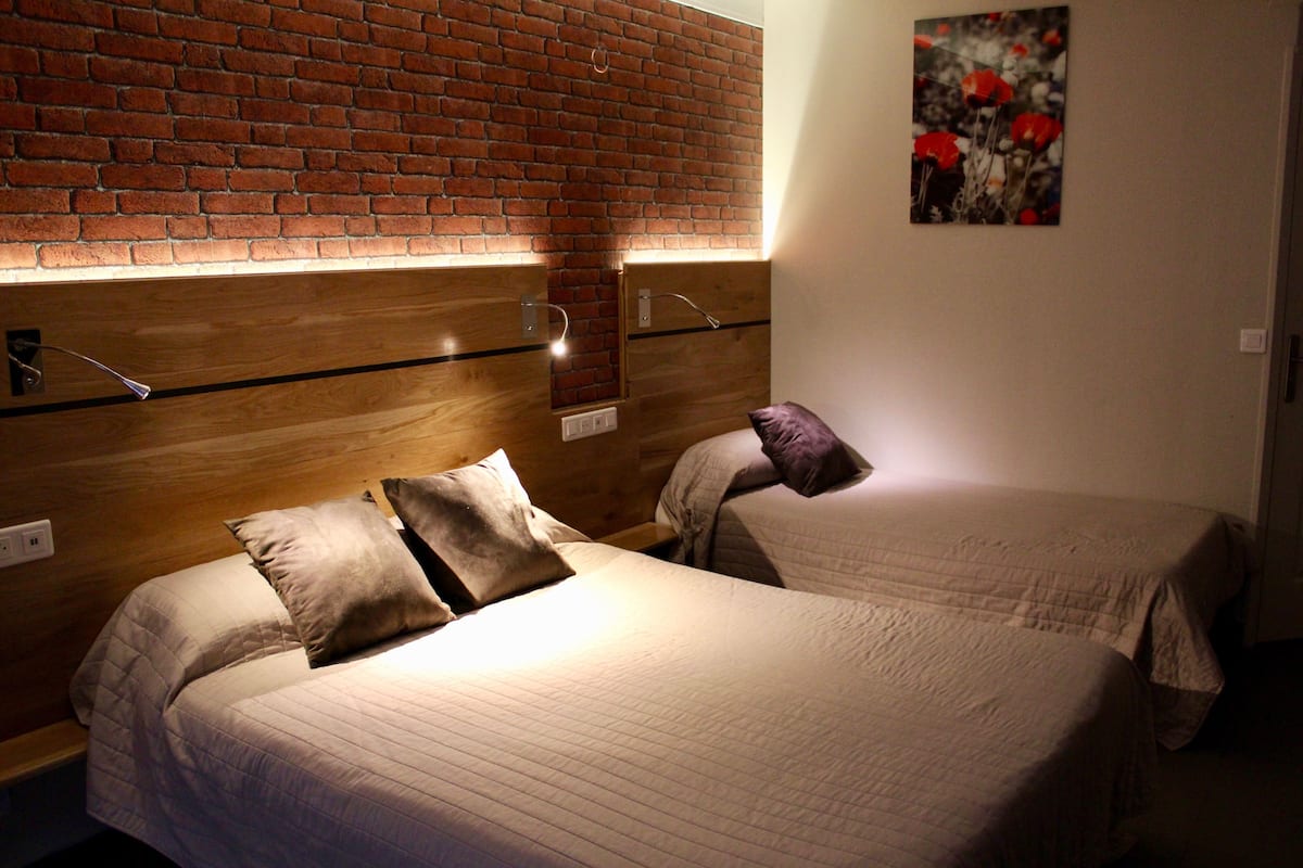 A hotel room with two beds, wooden headboards, and a brick wall.