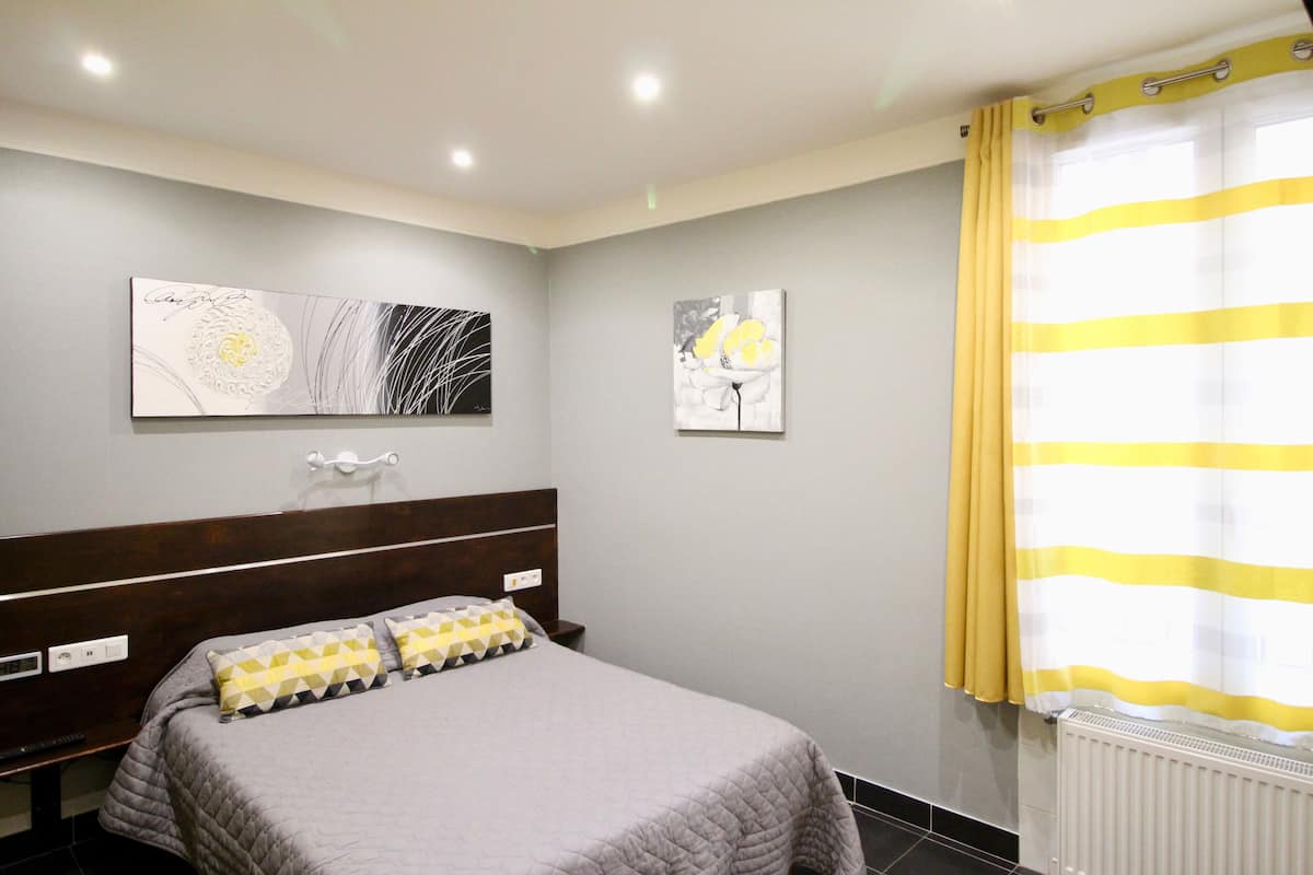 A bedroom with a bed, a nightstand, a wall-mounted lamp, and two framed artworks.