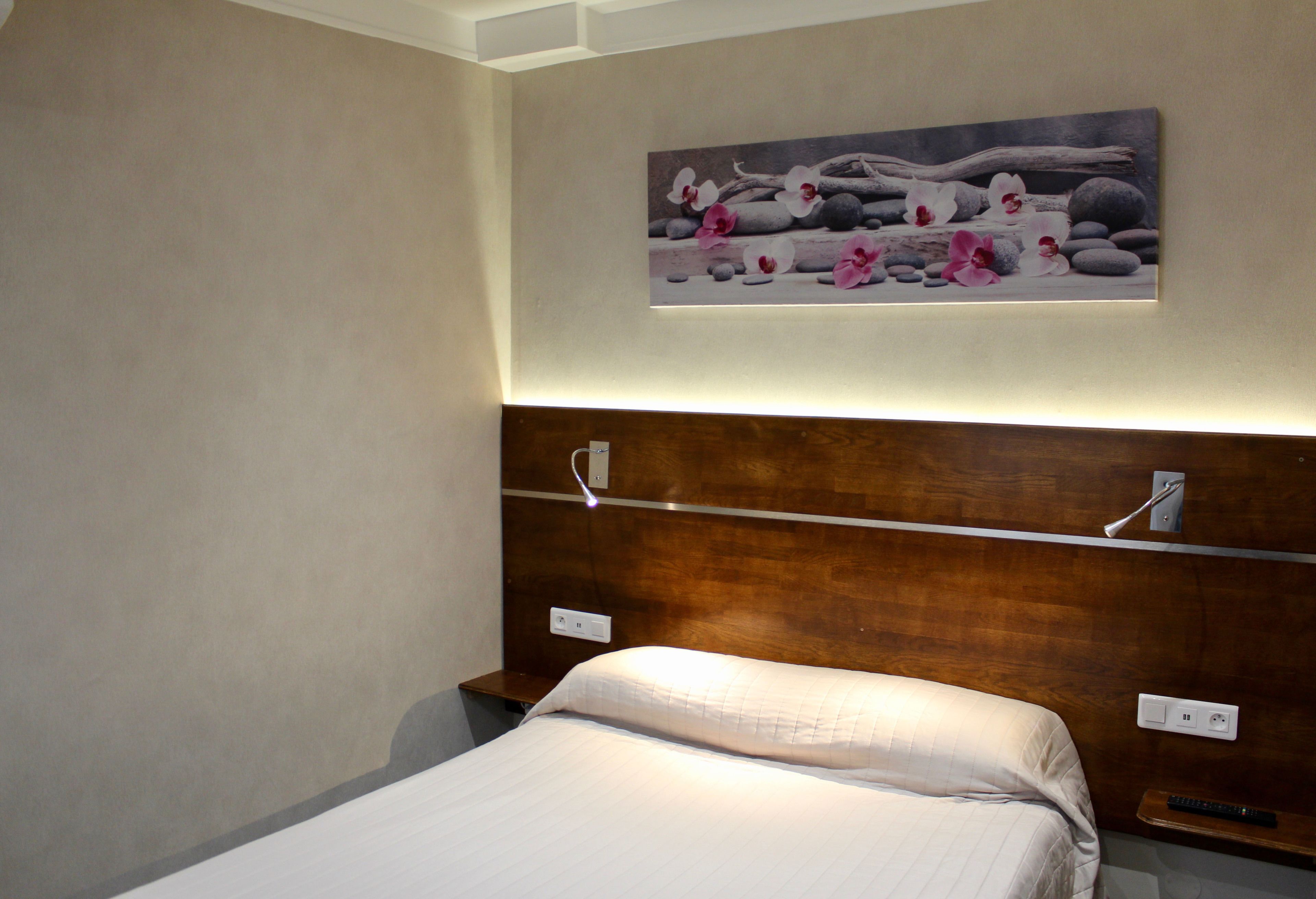 A hotel room with a bed, a wooden headboard, a painting of rocks and flowers, and a nightstand with a remote control.