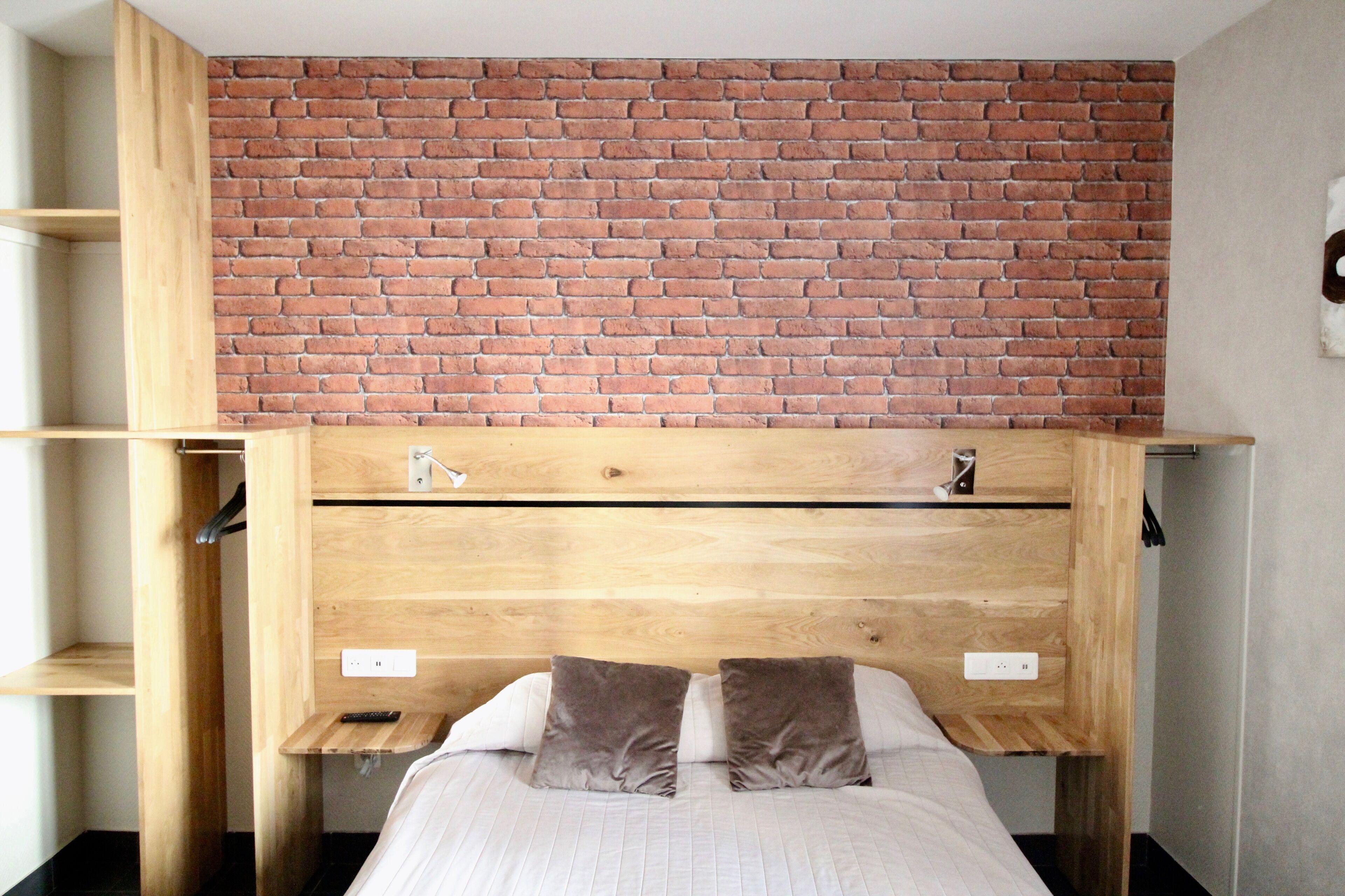 Una habitación con pared de ladrillo, cabecera de madera y cama con almohadas.
