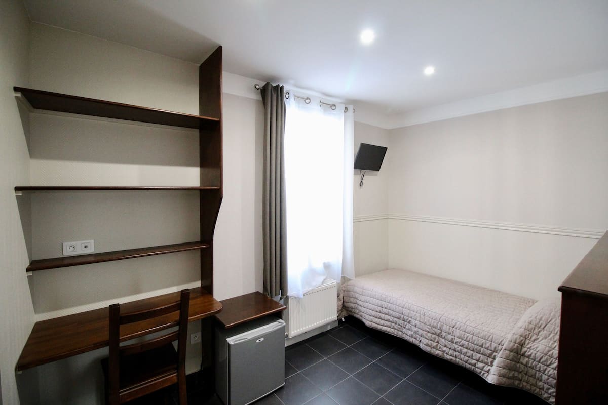 A small, neatly organized bedroom with a bed, a desk, a chair, and a TV mounted on the wall.