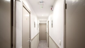 A narrow hallway with doors on both sides, a light fixture on the ceiling, and a door at the end. - Hôtel des Pyrénées (Paris)