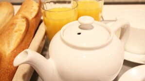 Une théière blanche avec un couvercle, deux verres de jus d’orange et une baguette sur une table.