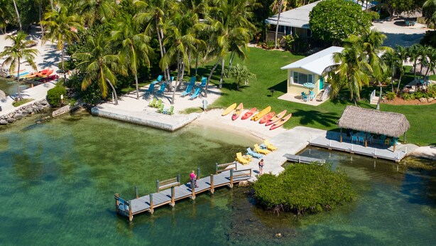 Vue aérienne d’un complexe hôtelier tropical avec des eaux cristallines, un quai et plusieurs kayaks.