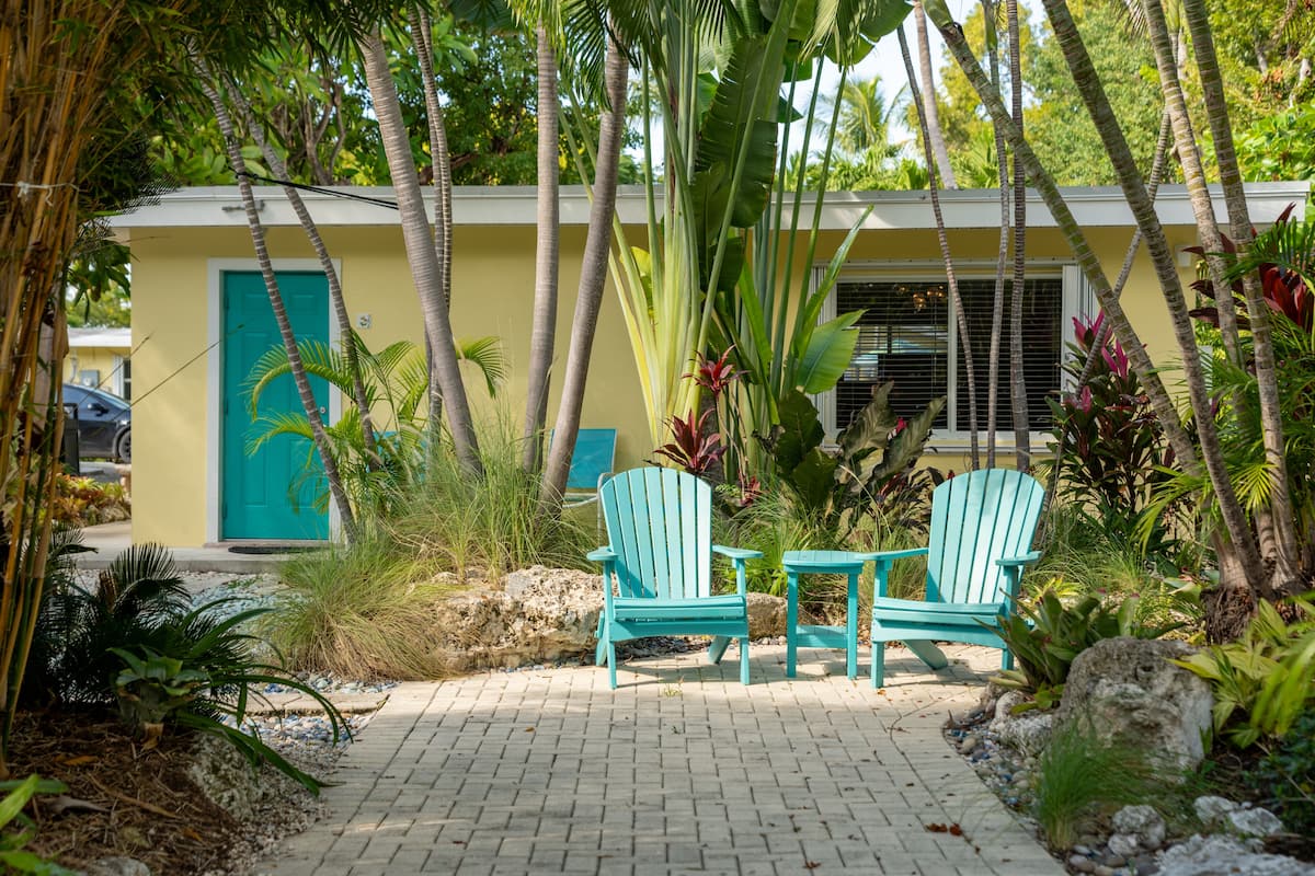 A pathway leading to a building with a turquoise door, two turquoise chairs, and a small table.
