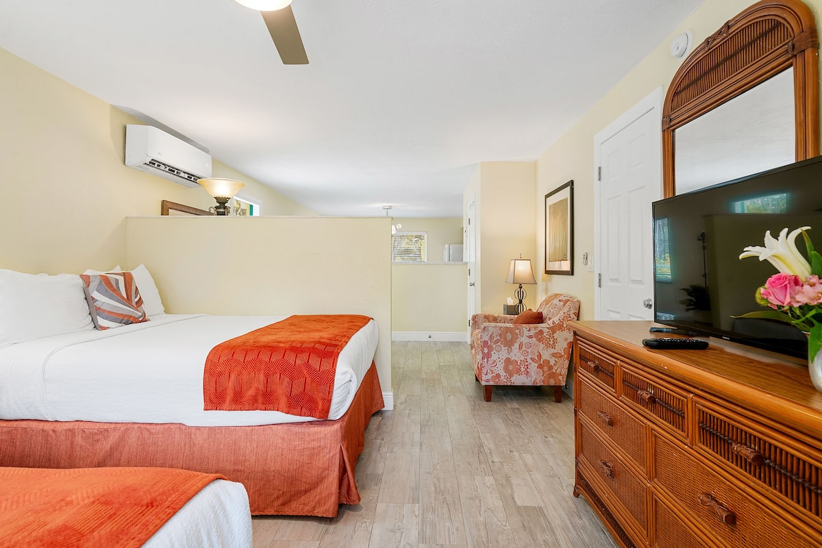 A hotel room with two beds, a television, a dresser, and a chair.