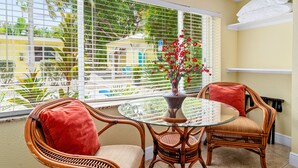 Un balcon avec des fauteuils en osier, une table en verre et un vase rempli de fleurs rouges.