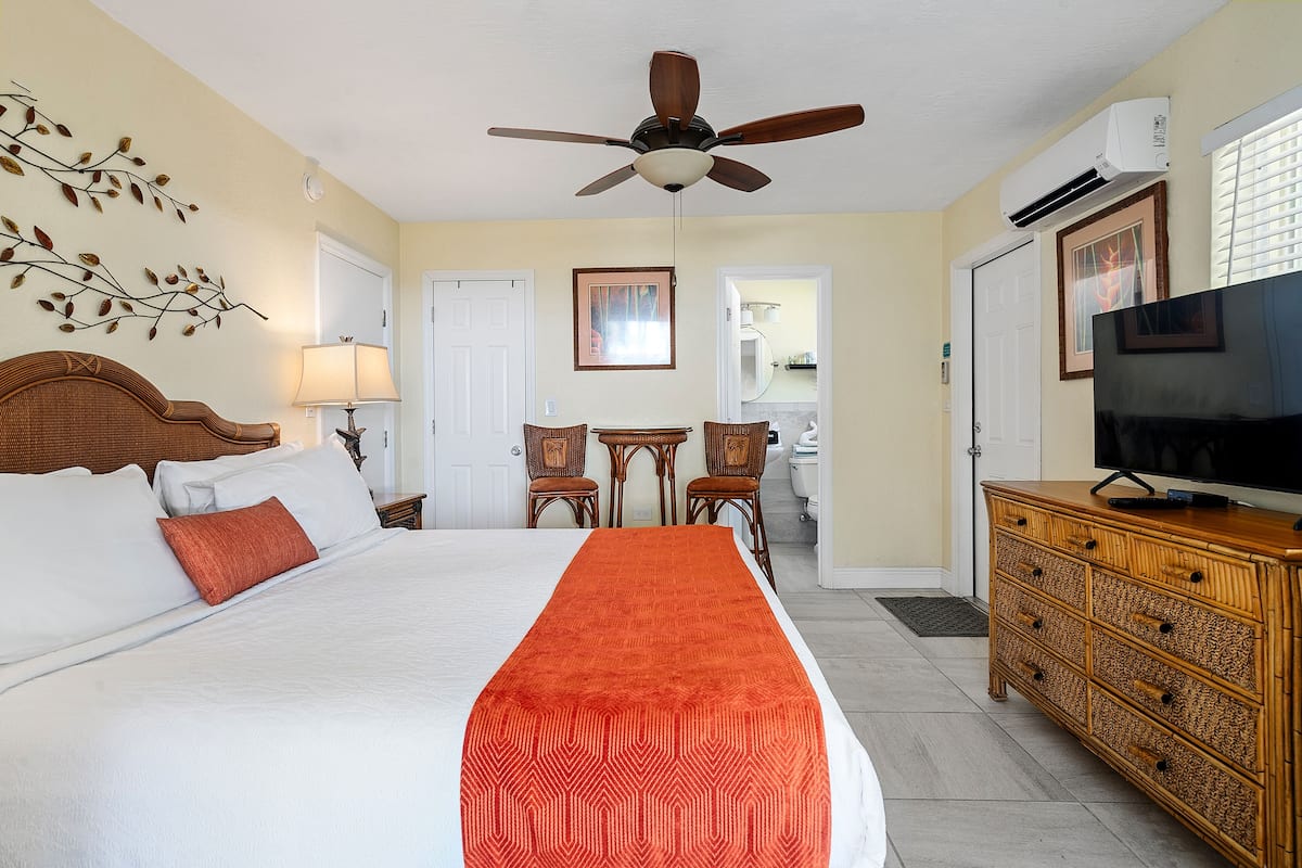 A hotel room with a bed, a television, a desk with chairs, and a ceiling fan.