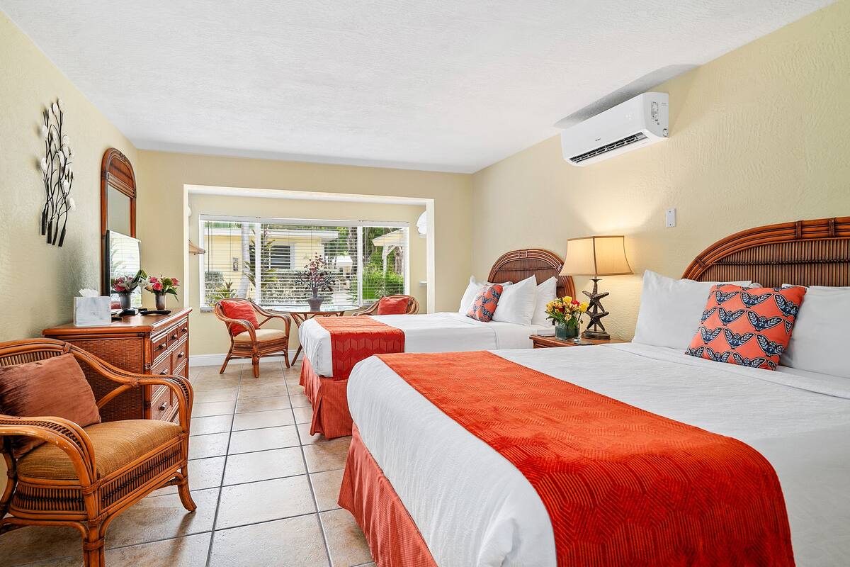 A hotel room with two beds, a sitting area with a chair, a dresser, and a view of the outdoors.