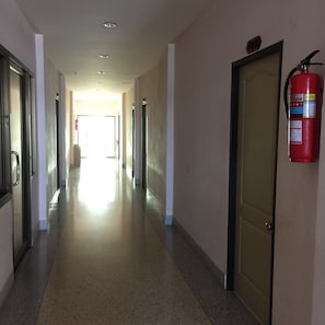 Un couloir avec des portes de chaque côté, un extincteur fixé au mur et une lumière vive au bout du couloir.