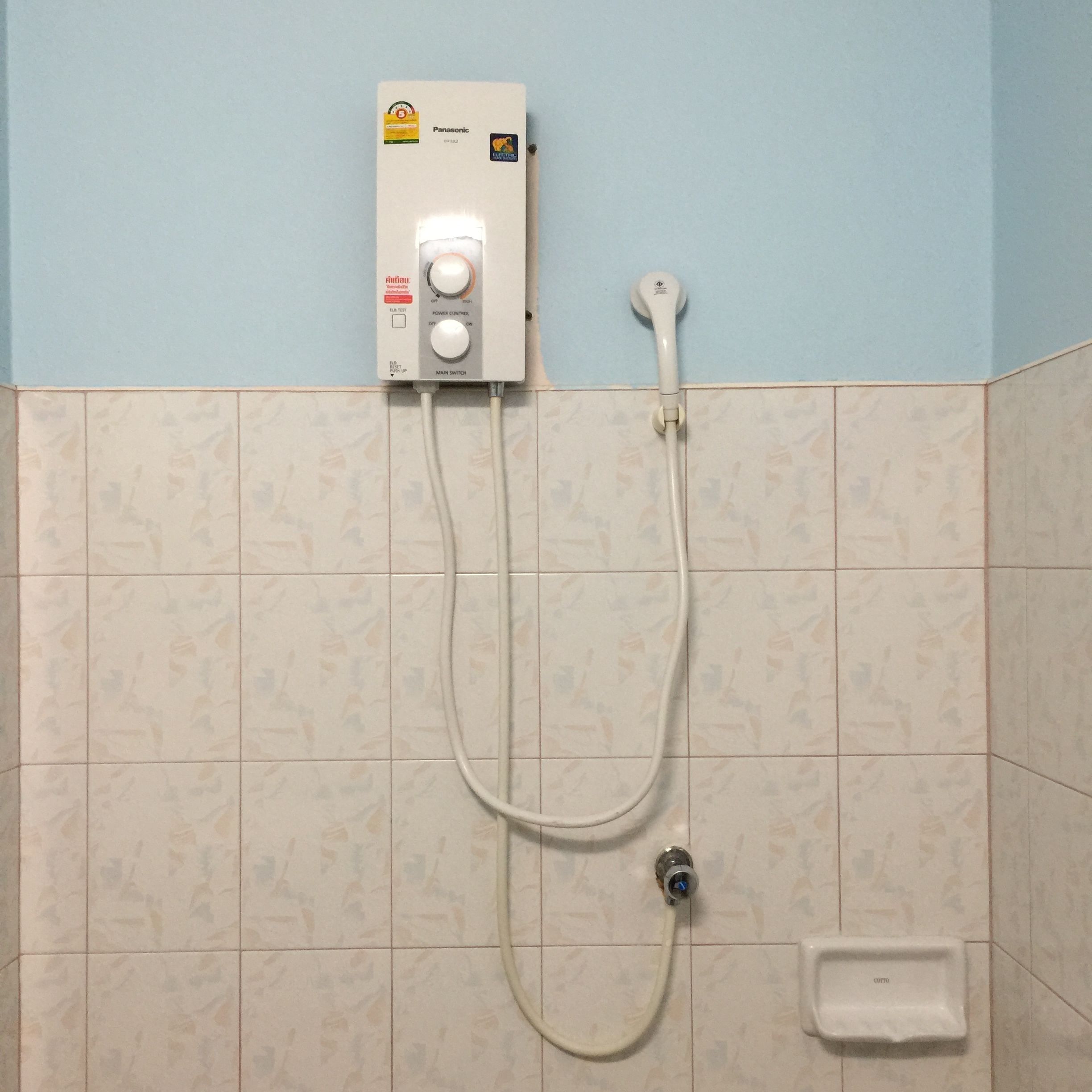 A bathroom with a wall-mounted shower control panel, a handheld showerhead, and a handheld bidet.