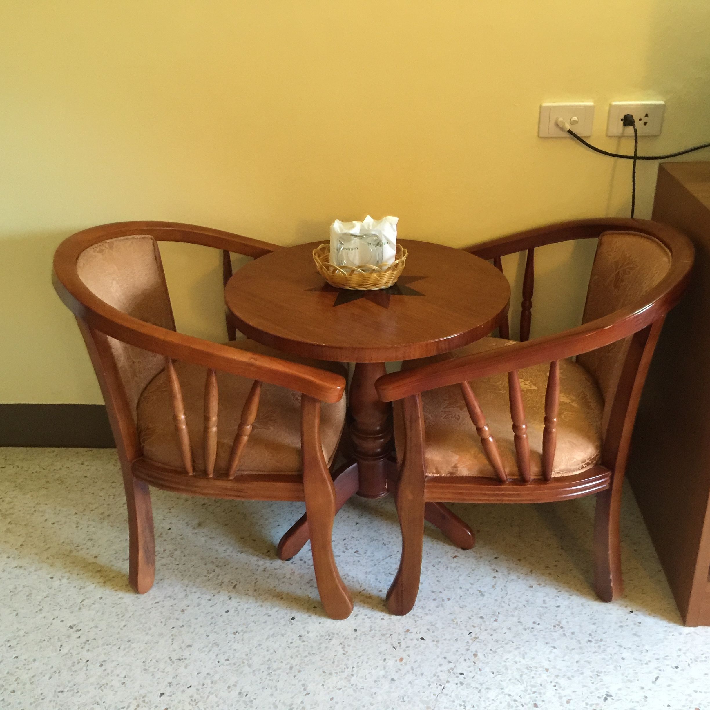 A wooden dining table with two chairs, a basket with items, and a power outlet on the wall.
