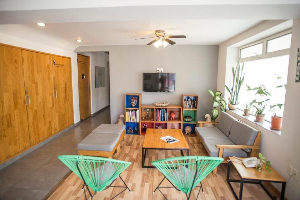 Una sala de estar moderna con un sofá, dos sillas verdes, una mesa de madera, un televisor y una estantería.