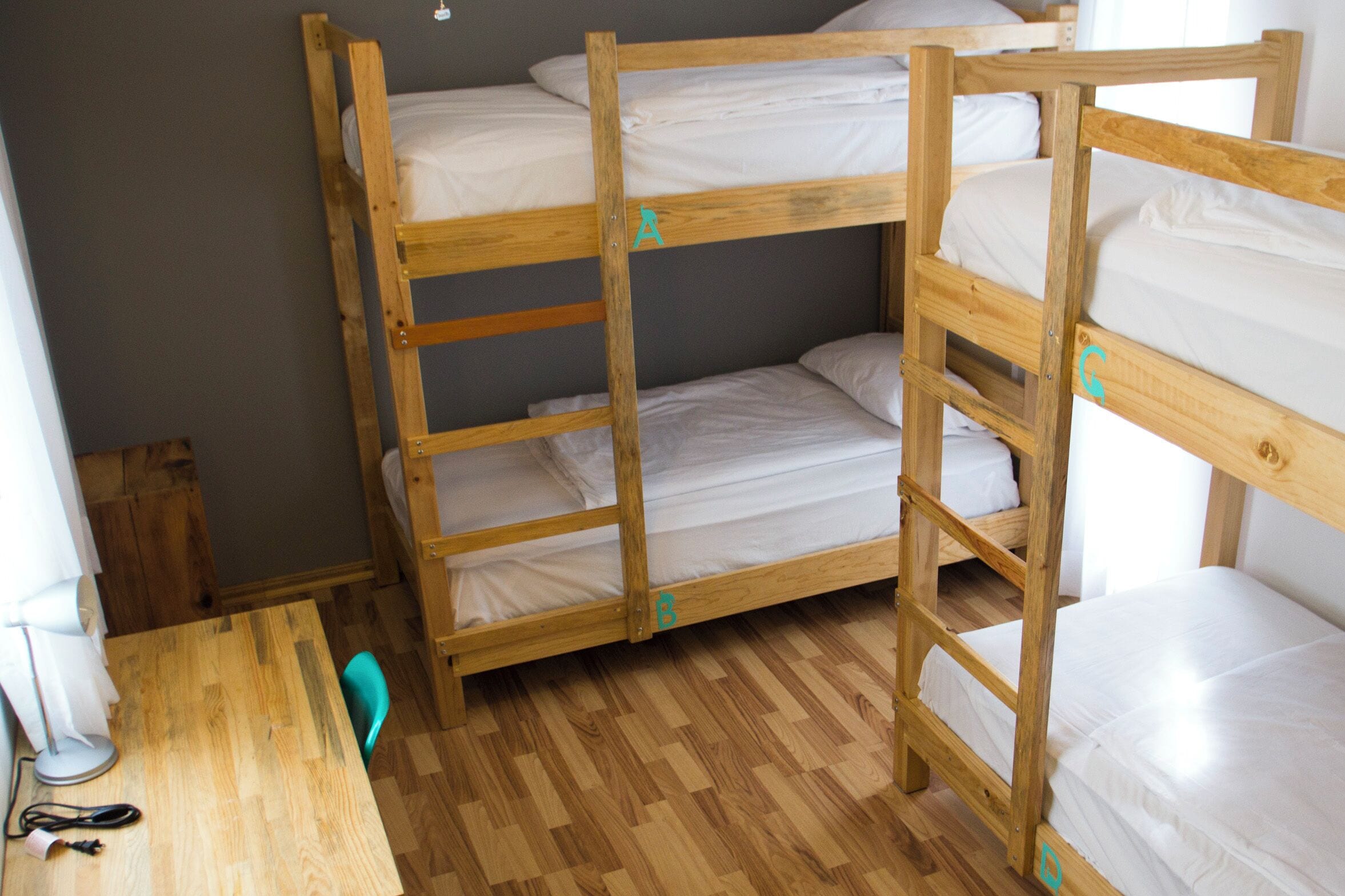 Habitación con literas de madera, una mesita pequeña y una silla.