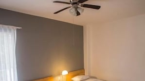 A hotel room with two single beds, a ceiling fan, a bedside table with a lamp, and wooden flooring. - Hostal Tres Central (Tuxtla Gutierrez)