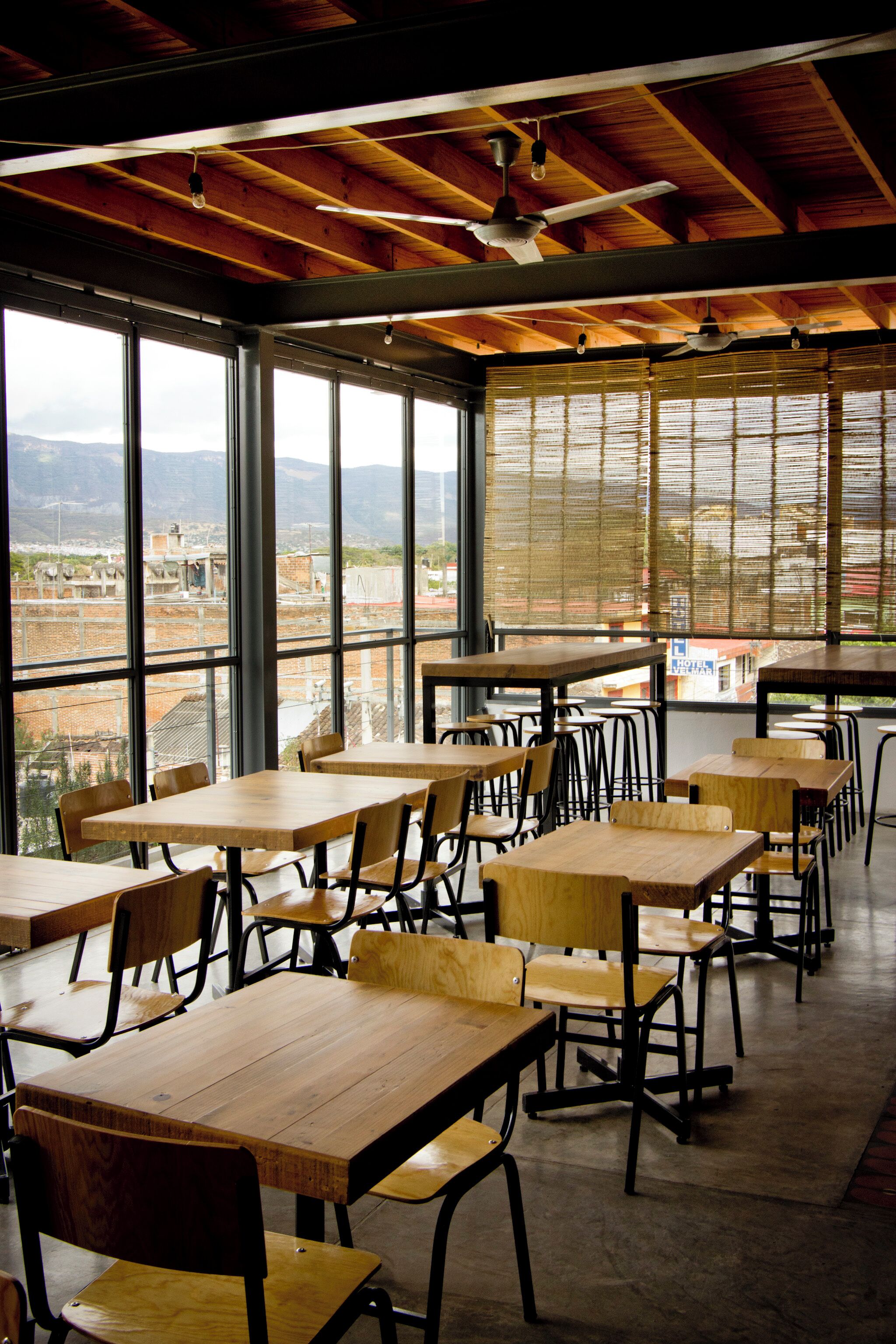 An indoor dining area with tables and chairs, large windows, and a view of the cityscape.