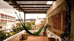A balcony with a green hammock, potted plants, and a view of buildings and hills. - Hostal Tres Central (Tuxtla Gutierrez)